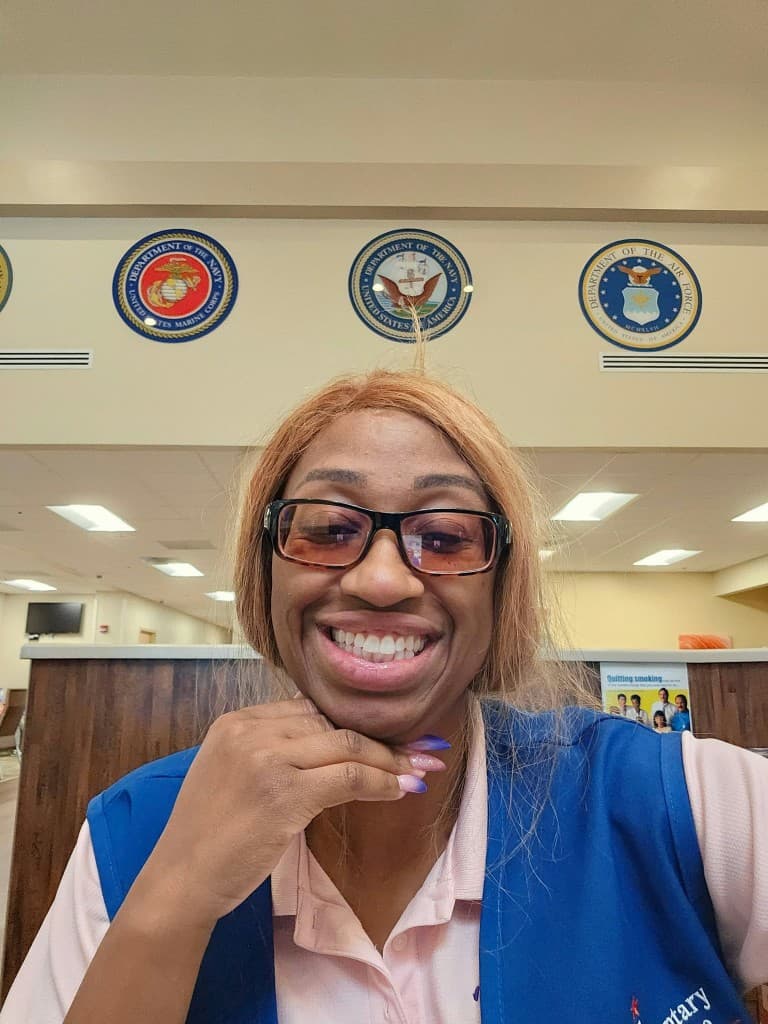 A Mu Alpha Rho founder smiling beneath the military service seals in a Veterans Affairs clinic lobby